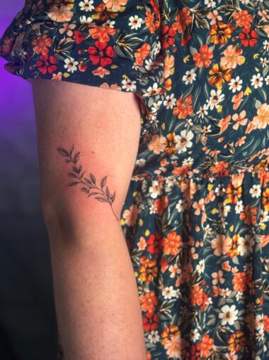 Delikatny tatuaż gałązki fine line na ramieniu